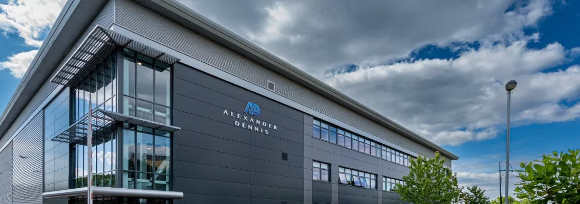 Modern Alexander Dennis manufacturing facility building with glass façade and company logo on the exterior.