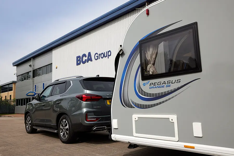 Grey SUV towing a Pegasus Grande SE caravan parked outside a BCA Group industrial building.